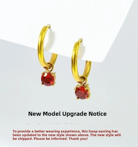 Detail of gold hoop earrings featuring polished finish and red round-cut zircon pendants