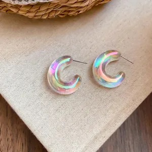 Iridescent acrylic U-shaped hoop earrings with colorful pearlescent finish on beige fabric