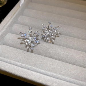 Macro detail of silver needle earrings with shimmering zircon and pearls on grey velvet