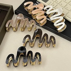 Set of five wavy hair claws in neutral colors with gold metal base on a stone surface