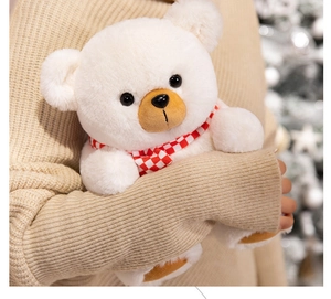 Close-up of cute white teddy bear with red plaid scarf being held in a festive setting