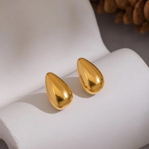Detailed close-up of golden teardrop earrings on a white stand with a soft background