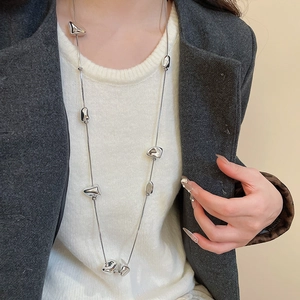 Detail of silver twisted square pendant necklace worn over a white sweater and grey blazer