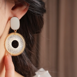 Close-up of model wearing gold-tone woven grid pattern hoop earring with white oval stud