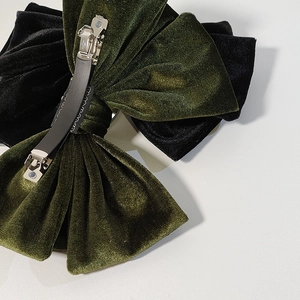 Detail view of green velvet bow hair clip showing silver metal spring clip with black grip