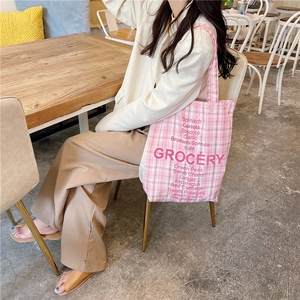 Chic pink checkered canvas tote bag with grocery text print worn in a cafe setting