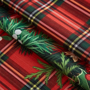 Detail of red Christmas plaid fabric featuring green leaves and white berry patterns