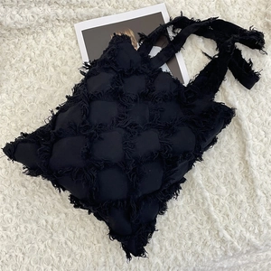 Detail of black quilted tote bag with fringe edges on white textured background