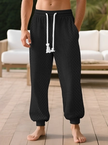 Detail of men's black waffle knit joggers with white drawstring and elastic cuffs
