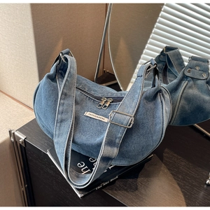 Detail of blue denim hobo bag with adjustable strap and metal zippers on books
