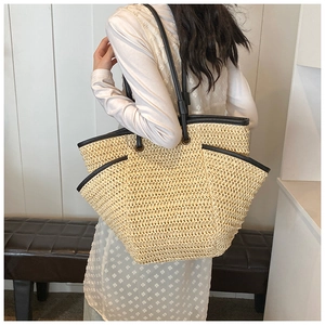 Detail of straw woven tote bag featuring beige texture and black PU leather strap details