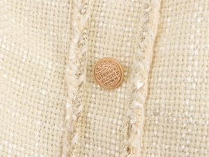 Macro shot of cream tweed fabric with metallic threads and a textured gold button detail