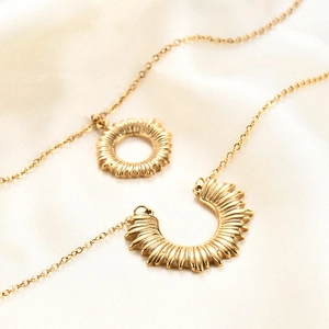 Macro shot of 18K gold plated sun and moon pendants on soft white silk background