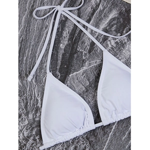 Detail of white triangle bikini top with adjustable halter neck ties on marble surface