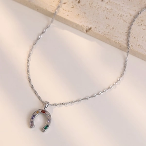 Silver horseshoe pendant necklace with colorful cubic zirconia on a textured stone
