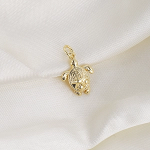 Macro shot of gold turtle pendant with starfish and shell relief on white silk background