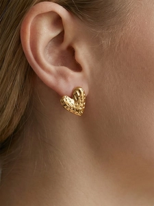Close-up of golden heart earrings with textured hammered finish on a female model