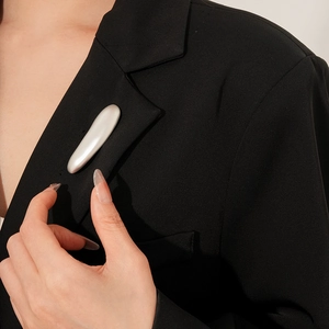 Minimalist silver-tone streamlined bar brooch displayed on a tailored black suit jacket
