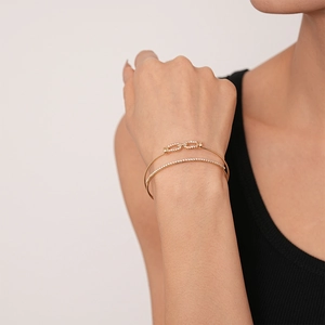 Detailed close-up of double-layered gold bracelet with pavé zircon and infinity link