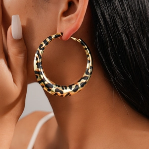 Macro side view of a large leopard print hoop earring with golden finish worn by a model