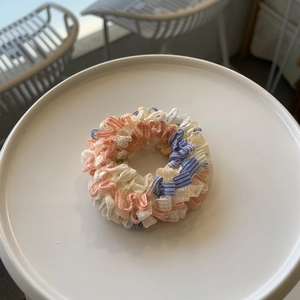 Détails de chouchous plissés en tissu rose, jaune et bleu pastel sur un plateau blanc
