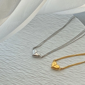 Close-up of gold and silver heart pendants on elegant snake chains with a soft background