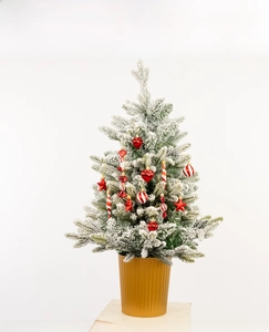 Detailed view of snowy desktop Christmas tree with red ornaments and golden base