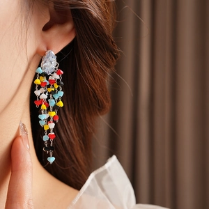 Detail of long tassel earrings with silver chains and colorful heart beads on a model