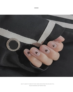 Detailed close-up of heart nail art stickers with minimalist black pattern on hand