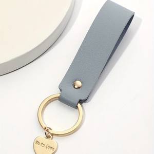 Detail view of light blue leather keychain with golden heart pendant engraved He is Love