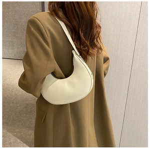 Chic beige half-moon baguette bag shown over the shoulder of a brown blazer
