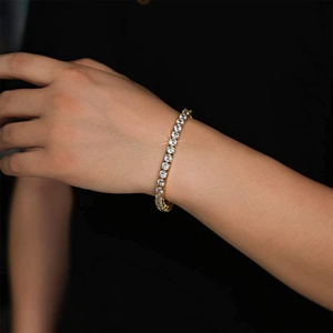 Primo piano di un bracciale tennis dorato con zirconi tondi indossato al polso su sfondo nero