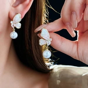 Detail of butterfly pearl earrings with gold metal frame and white crystal inlays