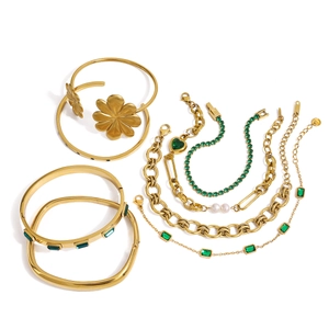 Set gioielli dorati con pietre color smeraldo, perle e bracciale a cuore su sfondo bianco