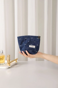 Close-up of blue denim cosmetic bag with white bow patterns and floral metal zipper