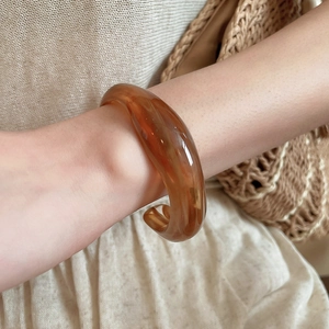 Close-up of amber translucent acrylic C-shaped cuff bracelet on a model's wrist