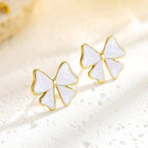 Elegant gold bow earrings with white enamel finish on a textured stone surface