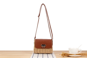 Close-up of brown leather flap and silver metal lock on a woven paper rope straw bag