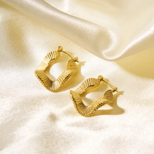 Detailed macro view of gold-plated wavy square earrings on a beige silk background