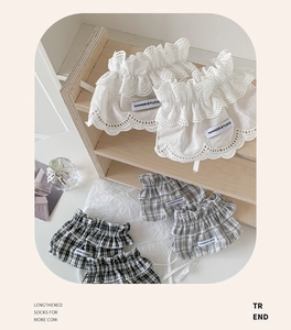 Detail of white lace and grey plaid leg warmers with ruffles and brand label on wood