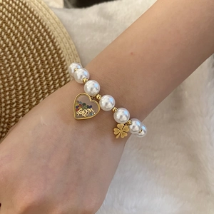 Detail of pearl bracelet with golden clover and heart pendant on wrist