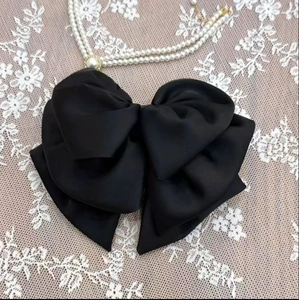 Detail of a large black satin bow hair claw with a central pearl on white lace background