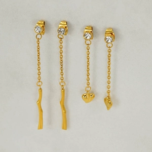 Macro detail of gold tassel drop earrings with wave charms and heart pendant accents