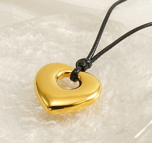 Detailed macro view of a polished golden heart-shaped hollow pendant on a black cord