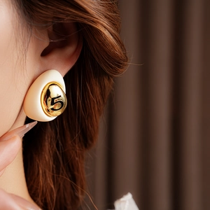 Detail shot of beige drop earrings with golden number 5 engraving worn by a model