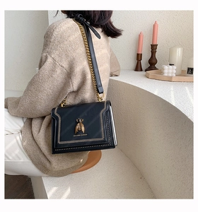 Detail of black leather bee crossbody bag featuring gold chain and V-shaped stitching