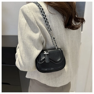 Close-up of mini black leather saddle bag with silver chain strap on a blazer model