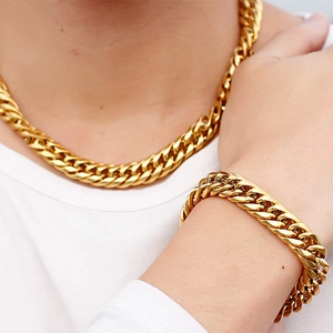 Polished golden stainless steel Cuban link necklace and bracelet set worn by a male model