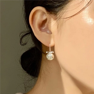 Close-up of 925 sterling silver bow pearl earrings worn by a model in a elegant style