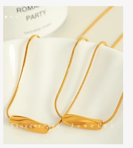 Close-up of golden geometric rectangular pendant necklace on a white ceramic plate